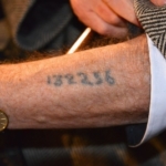Un survivant de la Shoah montrant le numéro tatoué sur son bras par les nazis (photo : Frankie Fouganthin - Own work, CC BY-SA 3.0, https://commons.wikimedia.org/w/index.php?curid=24277501).